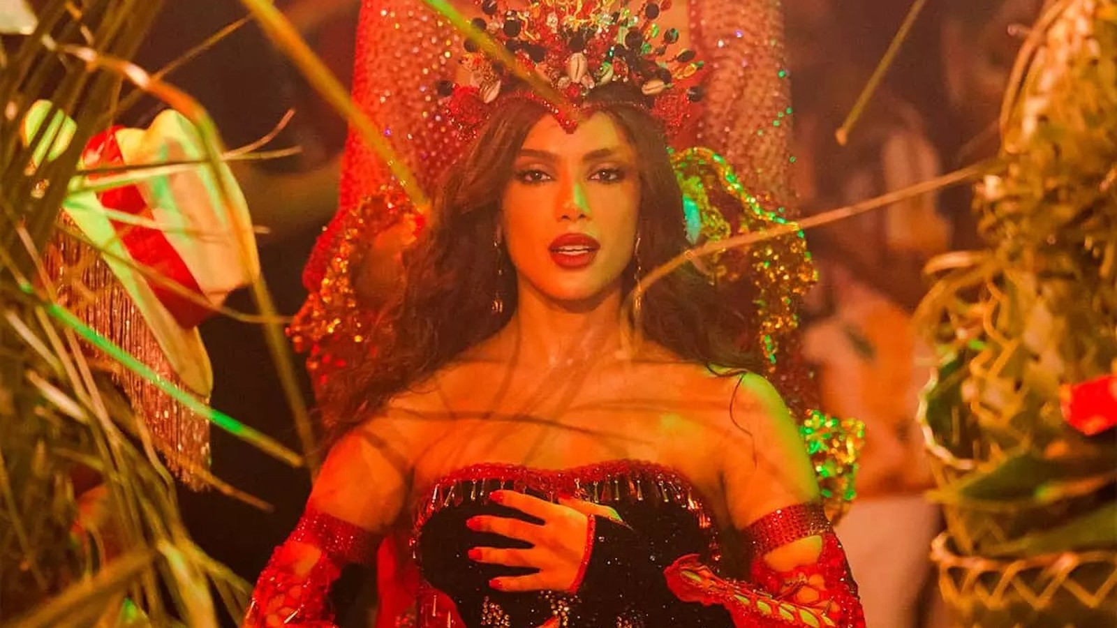 Cantora Anitta, com coroa e traje vermelho e preto, posa com a mão no peito