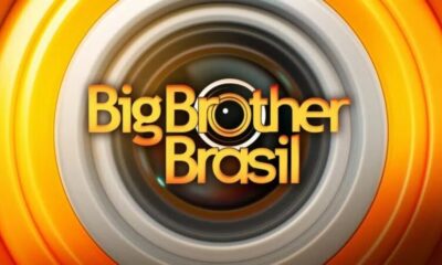 Logo Big Brother Brasil em laranja com câmera no lugar do 'o' em fundo de anéis concêntricos
