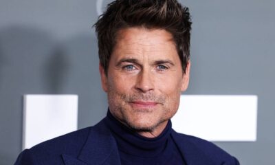 Close-up do ator Rob Lowe, com cabelo castanho, olhos azuis e barba rala, vestindo terno azul