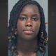 Mugshot de Aminata Amina Seck, mulher negra com tranças escuras e expressão neutra