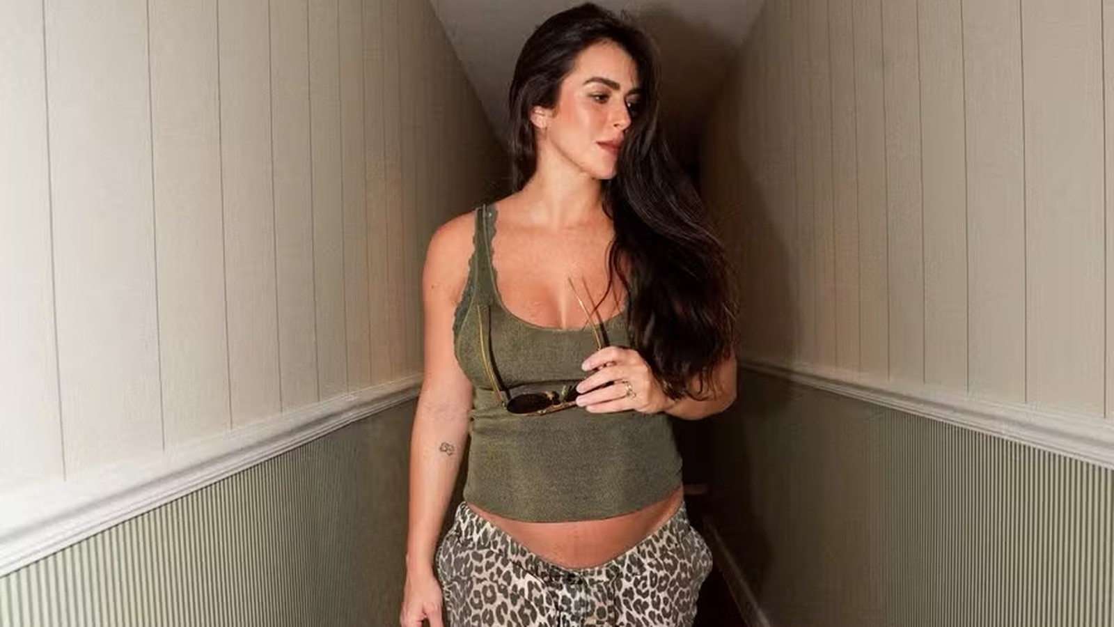 Mulher grávida de top verde e calça de oncinha segurando óculos escuros