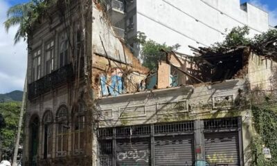 Fachada de prédio antigo com lado direito desabado, teto destruído e vegetação abundante
