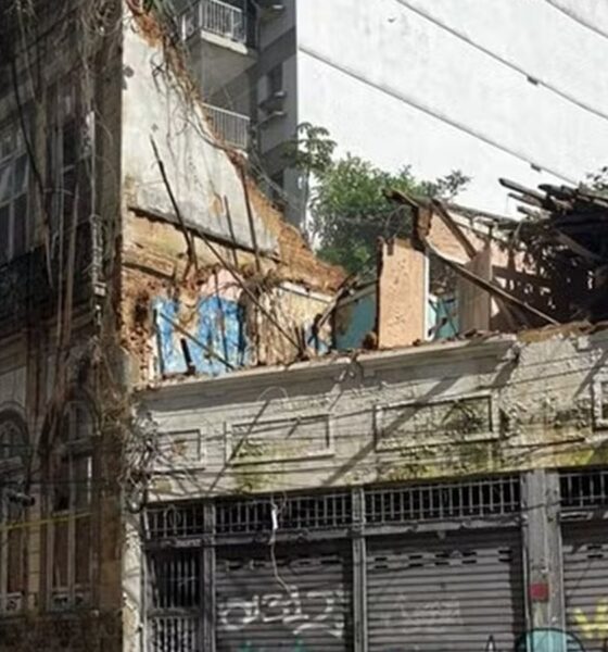 Fachada de prédio antigo com lado direito desabado, teto destruído e vegetação abundante