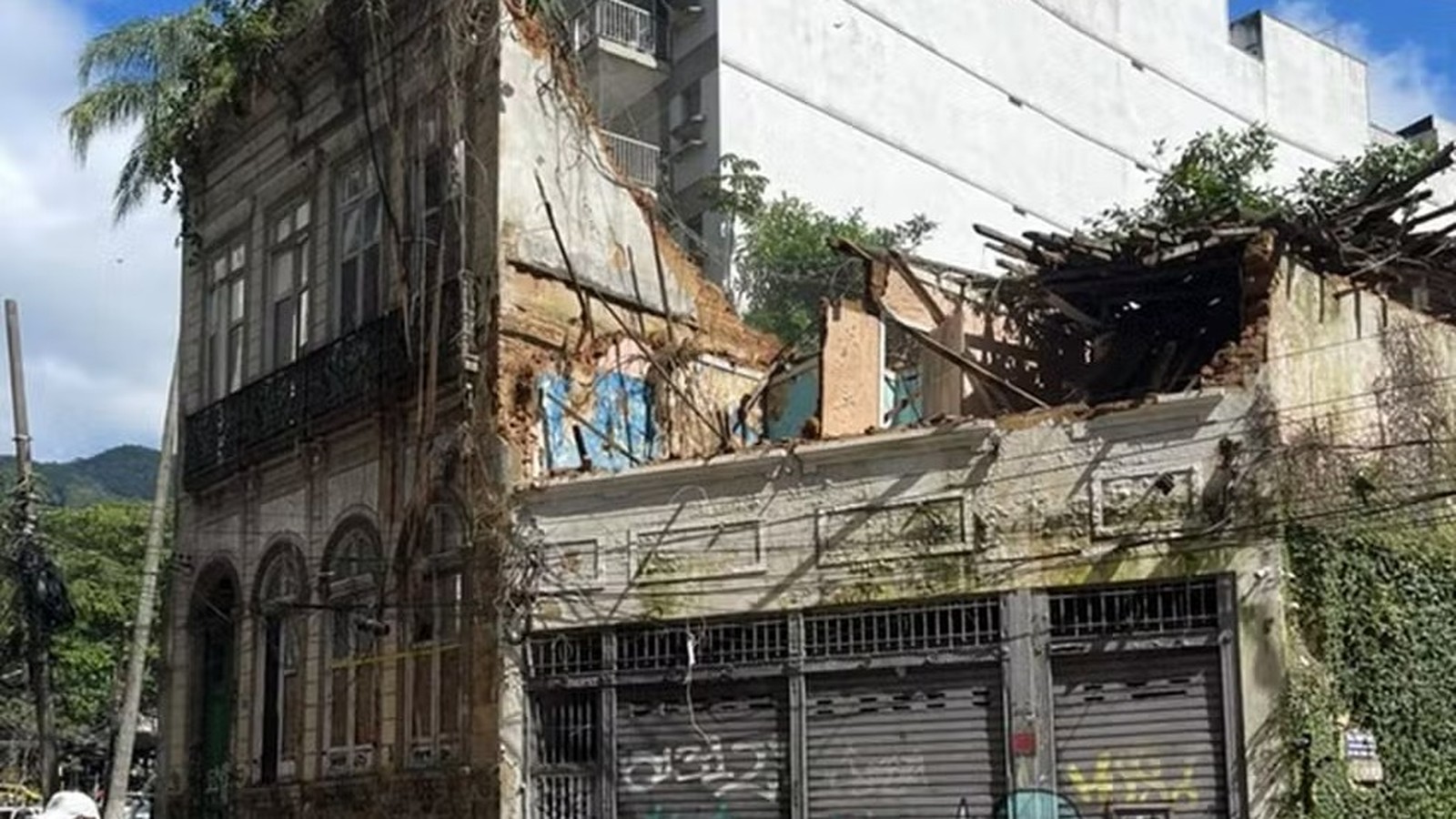 Fachada de prédio antigo com lado direito desabado, teto destruído e vegetação abundante
