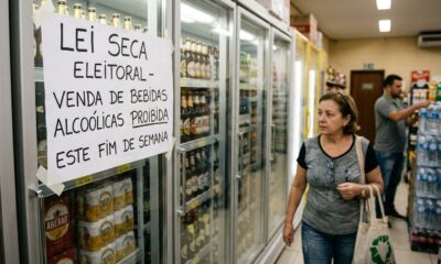 Placa 'Lei Seca Eleitoral' em refrigerador de bebidas alcoólicas em supermercado, com clientes