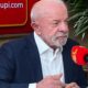 Luiz Inácio Lula da Silva em estúdio de rádio com microfone e painel 'radiotupi.com'