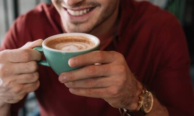 Homem sorrindo segura uma xícara azul de cappuccino com arte no leite