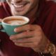Homem sorrindo segura uma xícara azul de cappuccino com arte no leite