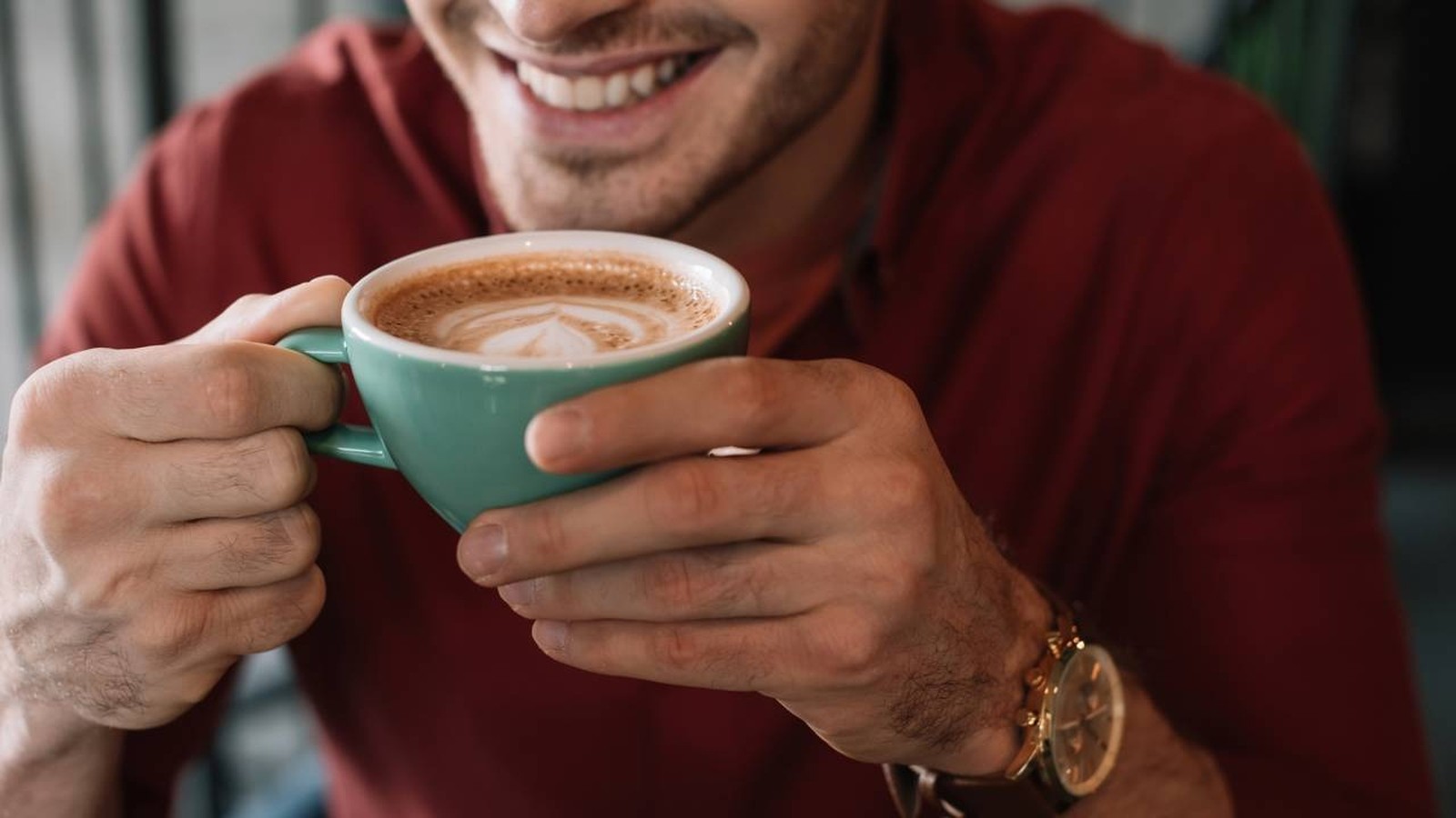 Homem sorrindo segura uma xícara azul de cappuccino com arte no leite