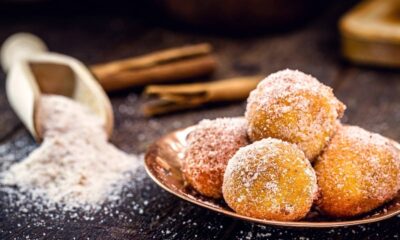 Bolinhos de chuva em prato de cobre, cobertos com açúcar e canela, sobre bancada de madeira