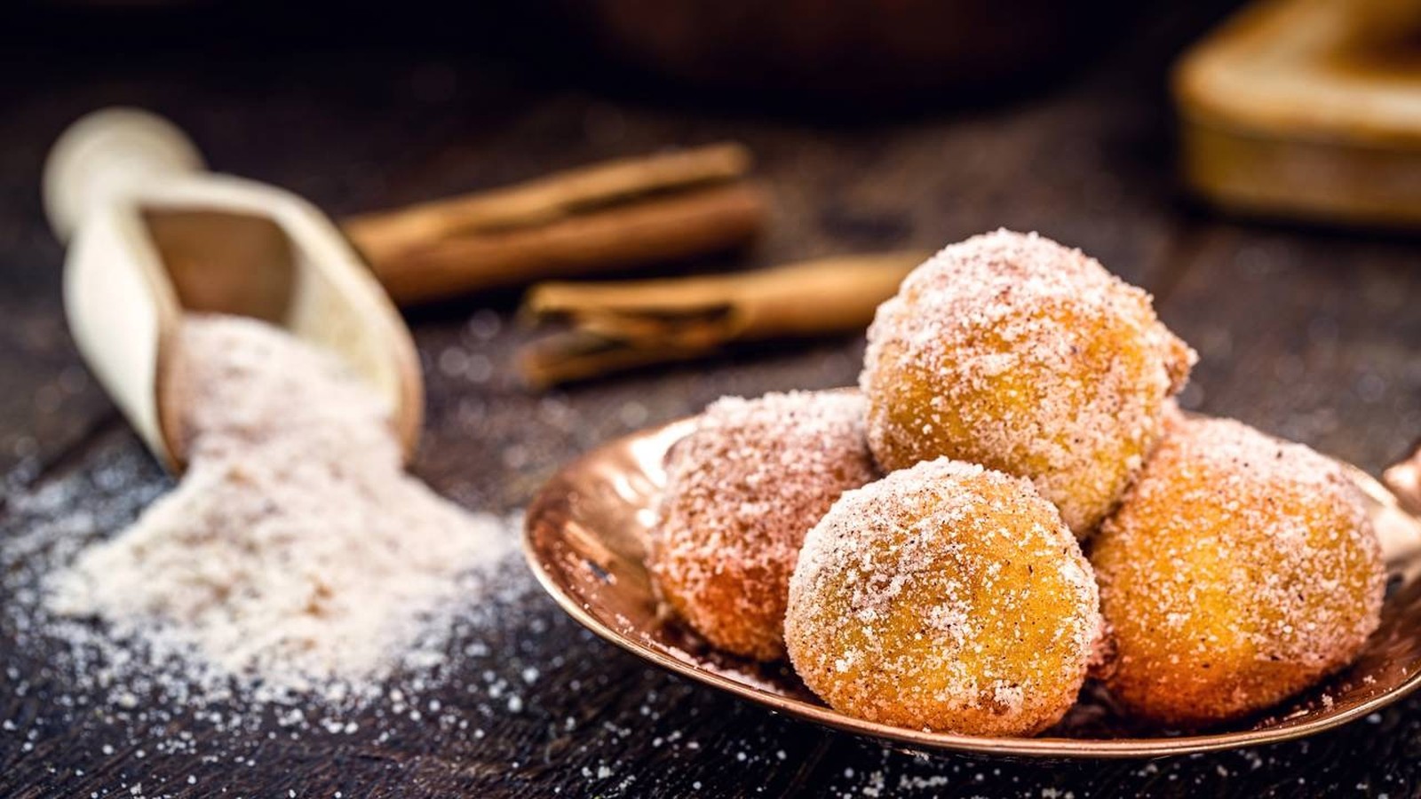 Bolinhos de chuva em prato de cobre, cobertos com açúcar e canela, sobre bancada de madeira