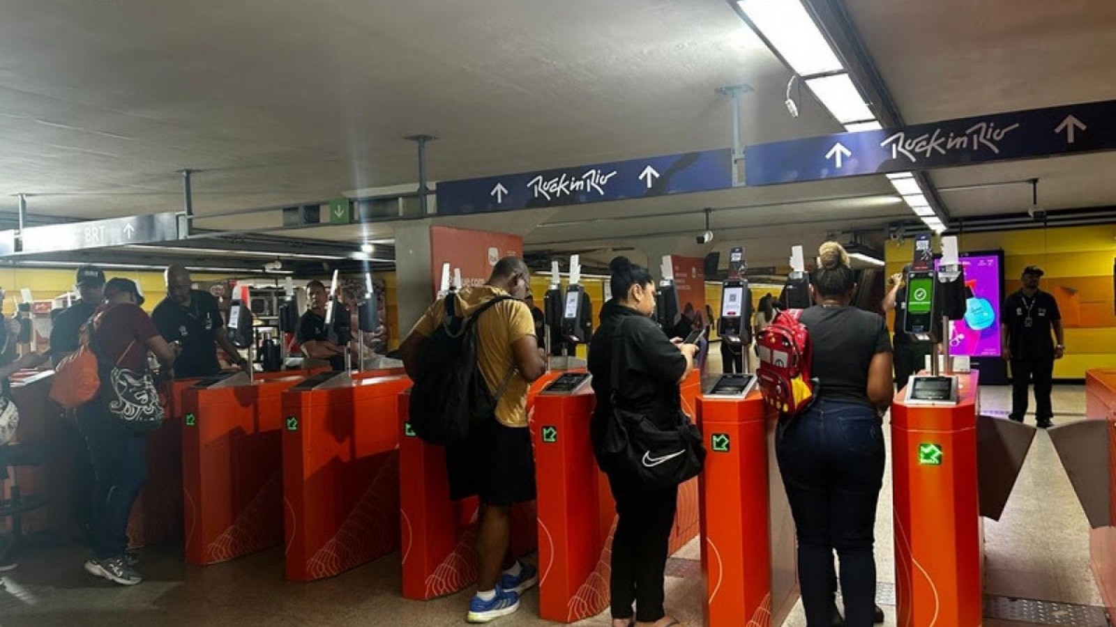 Muitas pessoas em catracas de estação com sinais indicando 'Rock in Rio' e 'BRT'
