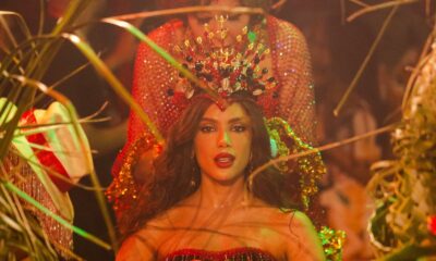 Anitta com coroa vermelha e dourada, maquiagem marcante, em meio a folhagens, durante coroação