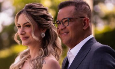 Casal sorrindo em close-up, homem de óculos e terno, mulher com penteado elaborado