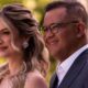 Casal sorrindo em close-up, homem de óculos e terno, mulher com penteado elaborado