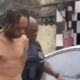 Homem de torso nu com dreadlocks escoltado por policial perto de viatura policial em rua