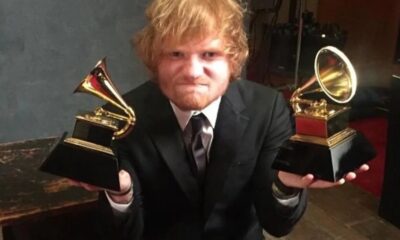 Ed Sheeran, ruivo e barbudo, em terno, segura dois troféus Grammy dourados