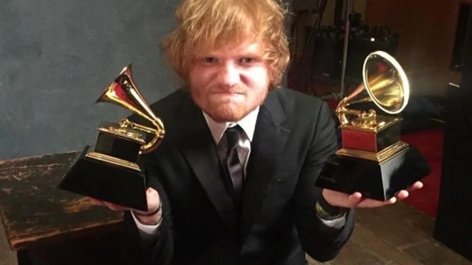 Ed Sheeran, ruivo e barbudo, em terno, segura dois troféus Grammy dourados