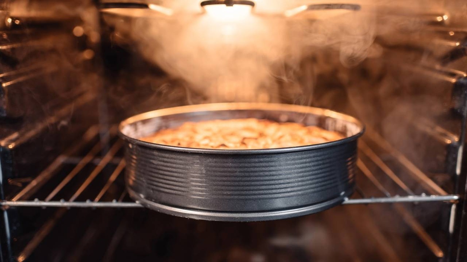 Bolo dourado em forma redonda assando em forno com vapor e luz acesa