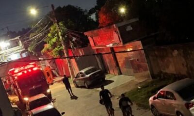 Caminhão de bombeiros com luzes vermelhas em rua noturna, pessoas e casa com brilho vermelho