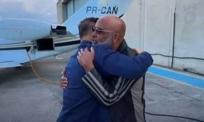 Dois homens abraçando em frente a uma aeronave azul com a inscrição PR-CAN na cauda
