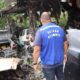 Homem de colete azul "DETRAN DESMONTE" em ferro-velho com carros e peças de automóveis