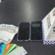 Dinheiro, diversos cartões bancários, dois celulares e placa da PMERJ sobre mesa escura