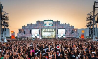 Show em palco iluminado para multidão com mãos levantadas, Itaú visível em pilares