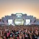 Show em palco iluminado para multidão com mãos levantadas, Itaú visível em pilares