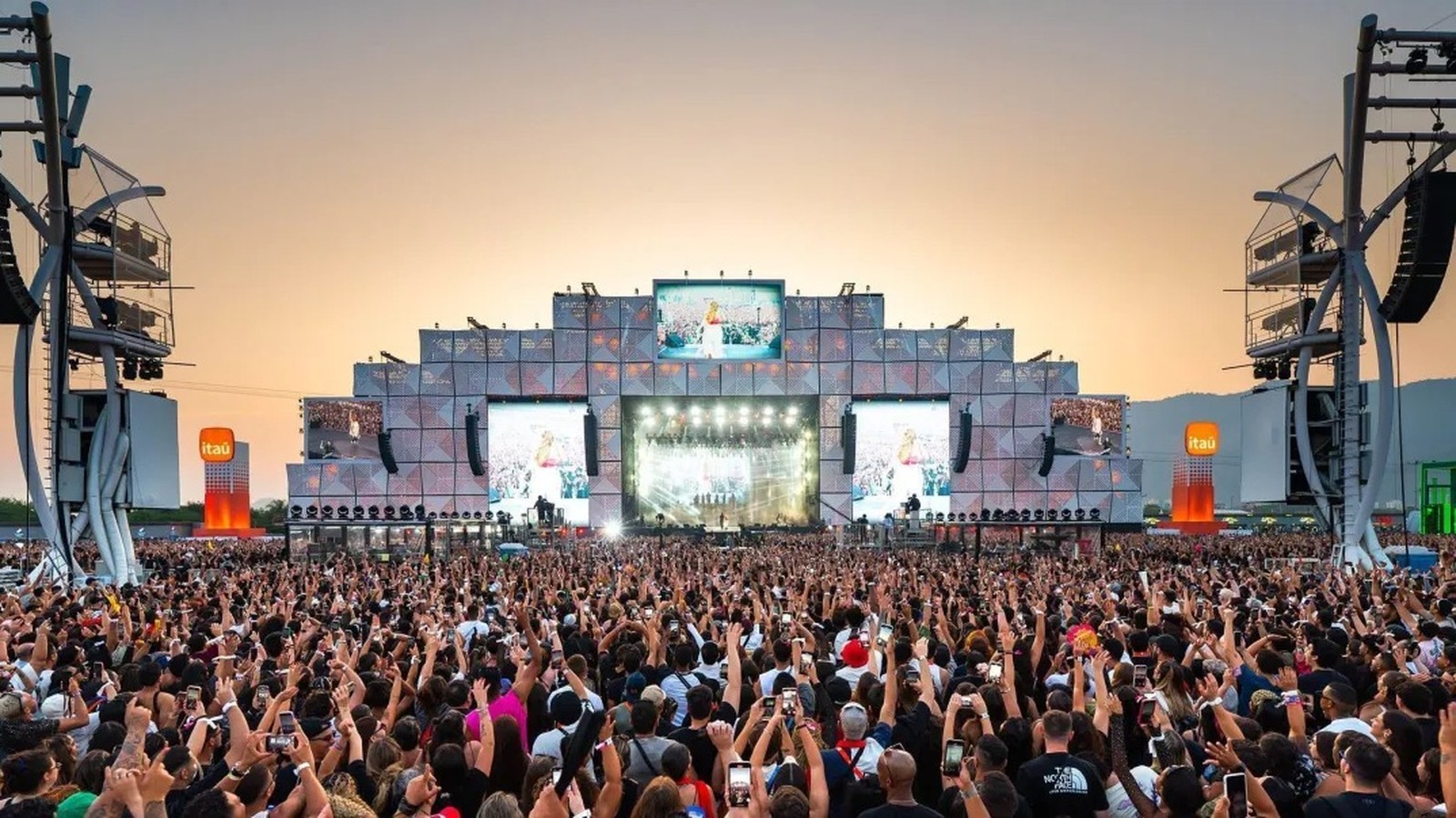 Show em palco iluminado para multidão com mãos levantadas, Itaú visível em pilares