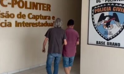 Dois homens em corredor da Polícia Civil. Placas 'DC-POLINTER' e 'BASE URANO' ao fundo