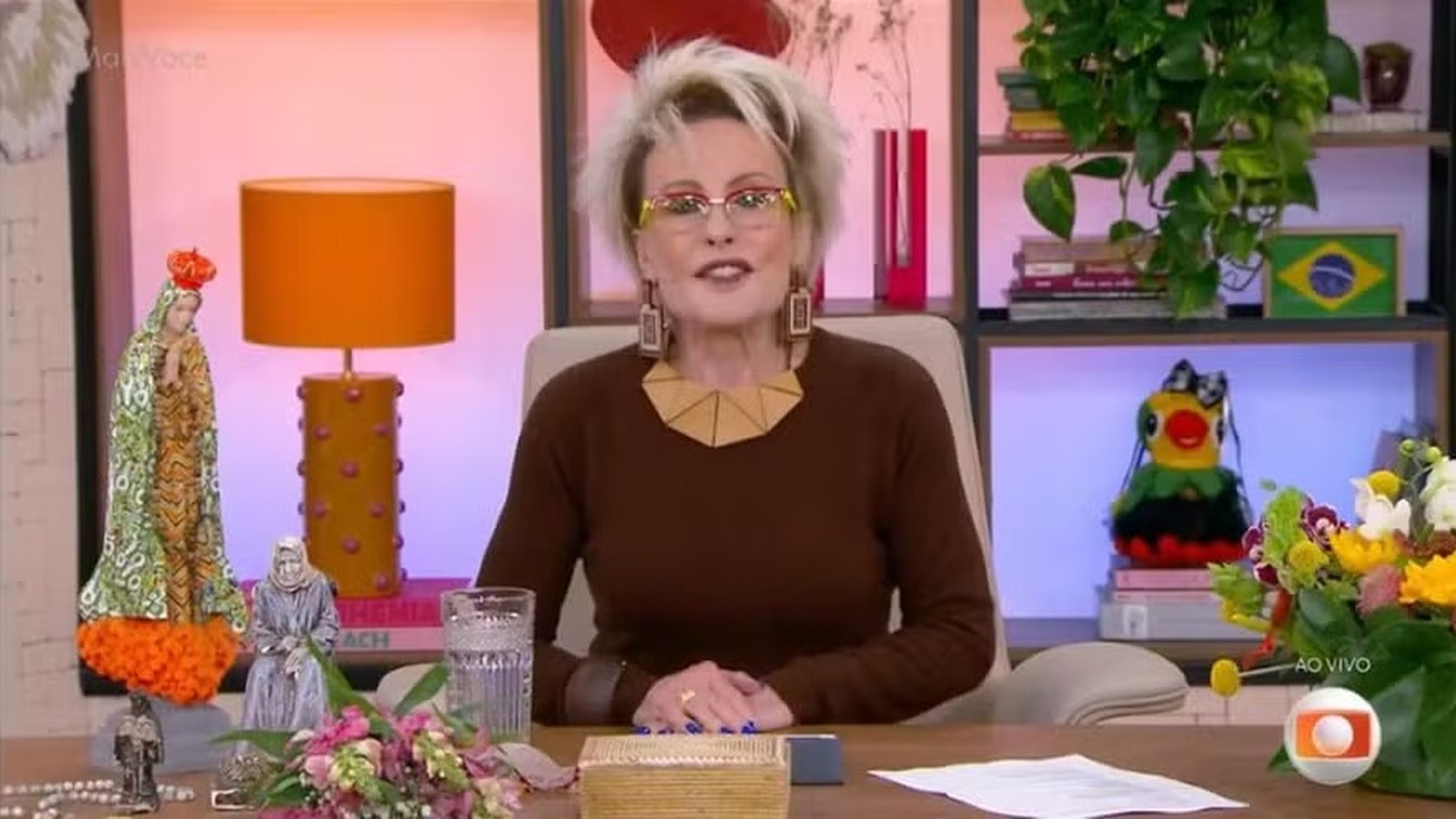 Ana Maria Braga, óculos, blusa marrom, sentada em estúdio, Louro José, estátuas, logo AO VIVO