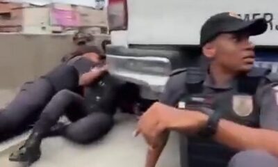 Policial fardado e alunos da PM abrigados no chão ao lado de veículo da corporação no RJ