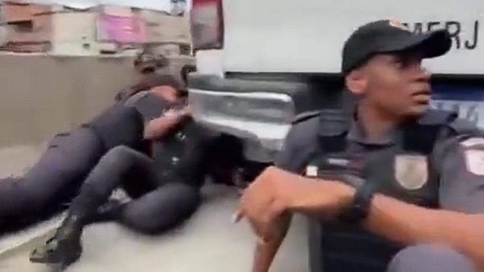 Policial fardado e alunos da PM abrigados no chão ao lado de veículo da corporação no RJ