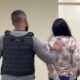 Homem em colete tático escolta mulher de cabelos escuros em corredor interno