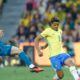 Dois jogadores, um do Brasil e outro adversário (VIANO), disputam a bola em campo de futebol