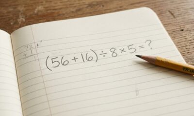 Caderno aberto com a expressão matemática (56 + 16) ÷ 8 × 5 escrita a lápis, sem revelar o resultado.