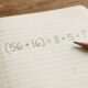 Caderno aberto com a expressão matemática (56 + 16) ÷ 8 × 5 escrita a lápis, sem revelar o resultado.