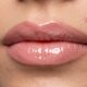 Lábios finos com contorno nude esfumado, batom rosado e gloss aplicado no centro para criar efeito de volume.