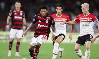 Jogador do Flamengo dribla a bola em jogo contra dois atletas do Estudiantes