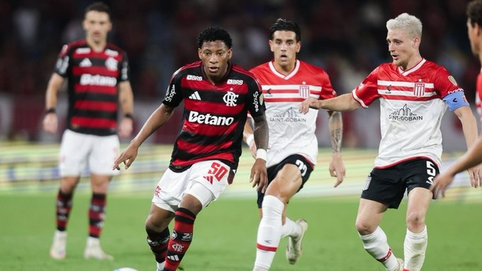Jogador do Flamengo dribla a bola em jogo contra dois atletas do Estudiantes