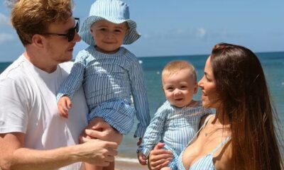 Homem, mulher e dois bebês na praia, todos sorrindo e usando roupas listradas
