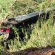 Ônibus escuro danificado, virado em ribanceira com vegetação e terra