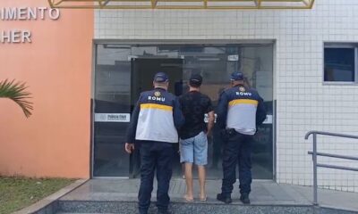 Dois guardas ROMU escoltam homem para Delegacia Civil com letreiro "Mulher" e logo