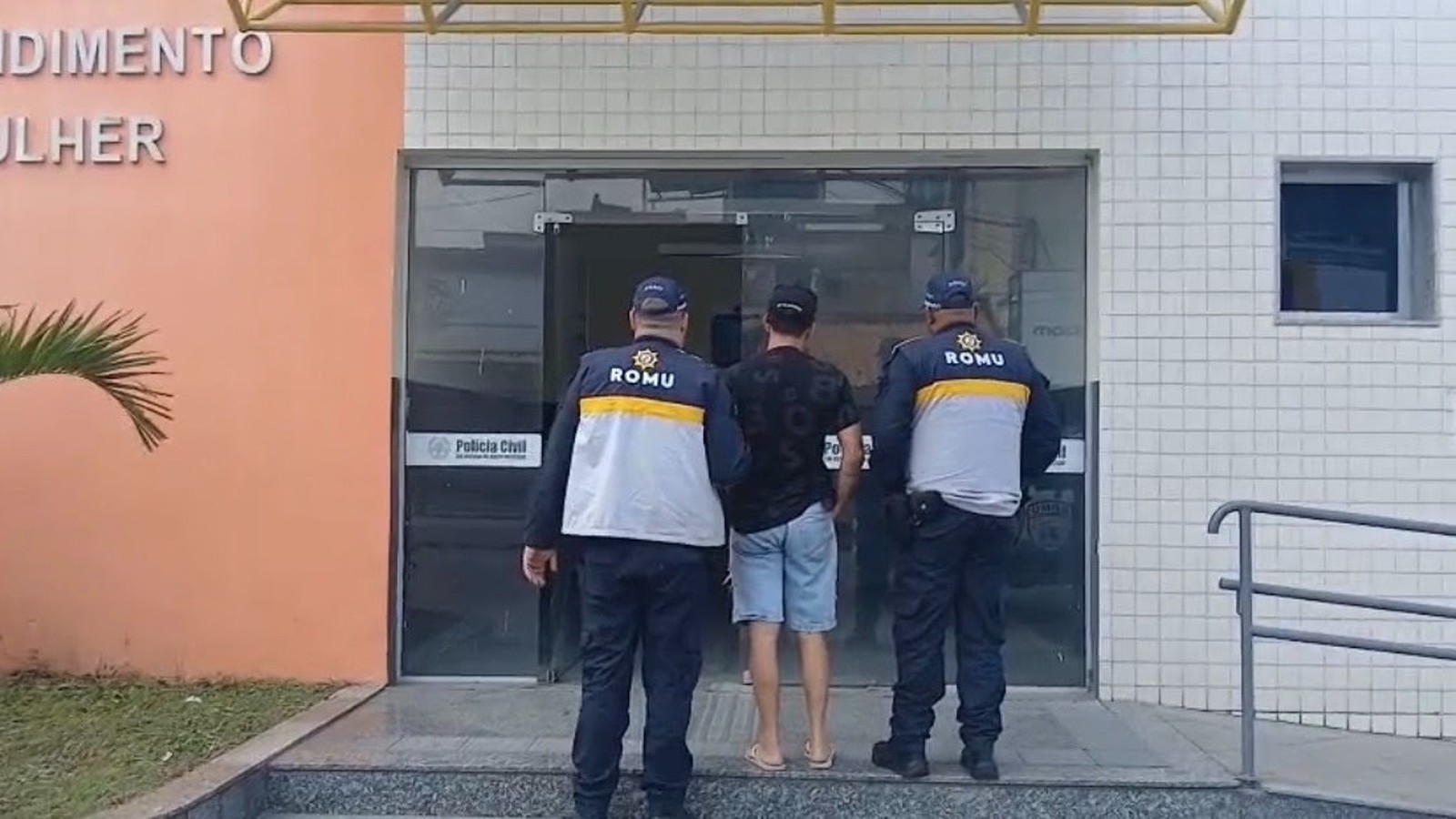 Dois guardas ROMU escoltam homem para Delegacia Civil com letreiro "Mulher" e logo