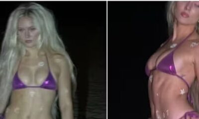 Zara Larsson com cabelos loiros e biquíni roxo, pele molhada com decorações de estrela, em ambiente escuro