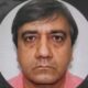 Rosto de homem, cabelo escuro e liso, camisa rosa, em foto de perfil circular