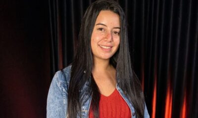 Mulher jovem com cabelos escuros e jaqueta jeans sorri para a câmera