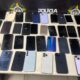 Muitos celulares de diversas marcas e modelos, alguns com telas quebradas, sobre uma mesa policial