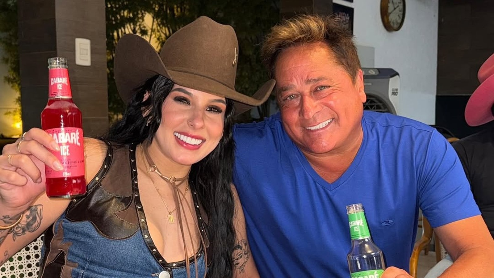 Ana Castela de chapéu e Leonardo de camisa azul sorrindo, segurando garrafas de Cabaré Ice